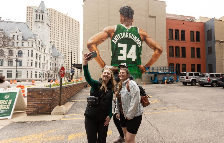 Two guests standing next to the Giannis Bucks mural in Milwaukee, Wisconsin